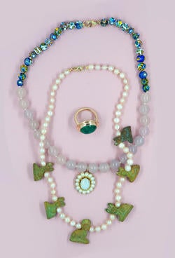 Two beaded necklaces and a ring against a pale purple background.